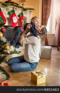 Happy smiling mother and 1 year old baby son posing at Christmas tree