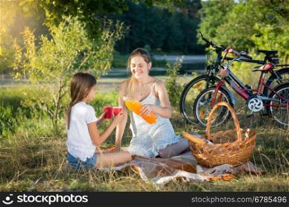Happy smiling mother and daughter drinking orange juice at picnic