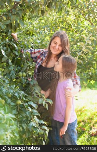 Happy smiling mother and daughter posing at apple garden at sunny day