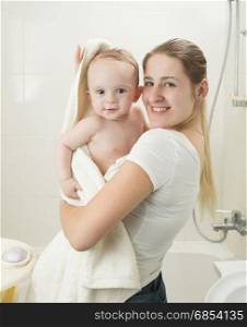 Happy smiling mother wiping her baby with towel after having bath