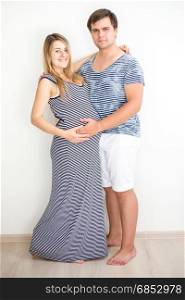 Happy smiling pregnant couple in striped clothes posing against white wall