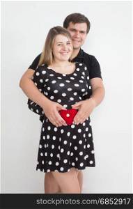 Happy smiling pregnant couple posing with small heart