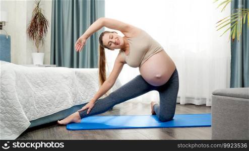 Happy smiling pregnant woman doing sportrs stretching and fitness exercises on mat at big window in morning. Concept of healthcare and sports during pregnancy.. Happy smiling pregnant woman doing sportrs stretching and fitness exercises on mat at big window in morning. Concept of healthcare and sports during pregnancy