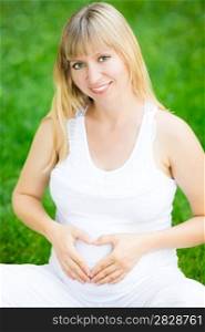 Happy smiling pregnant woman holding hands on belly in shape of heart