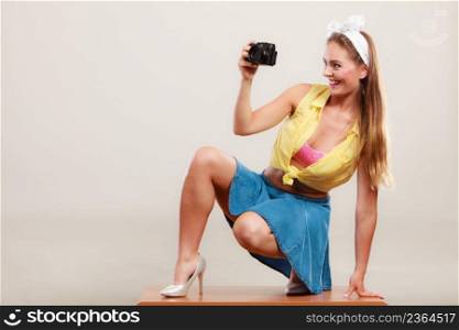 Happy smiling prettyπn up girl wearing hairband bow, skirt and high heels taking photoπcture with camera. Attractive gor≥ous young retro woman photograφng.