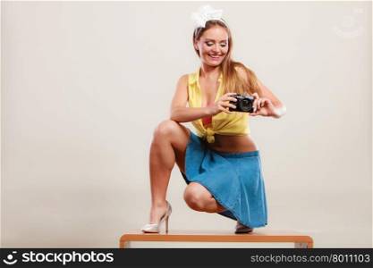 Happy smiling pretty pin up girl wearing hairband bow, skirt and high heels taking photo picture with camera. Attractive gorgeous young retro woman photographing.