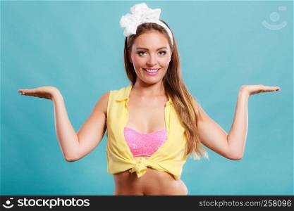 Happy smiling pretty pin up girl wearing hairband bow with empty hands for copy space. Attractive gorgeous young retro woman posing in studio on blue background.