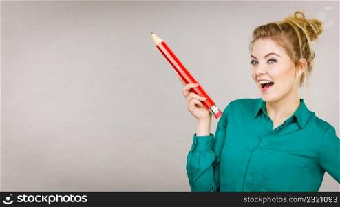 Happy smiling student looking woman wearing green shirt holding big oversized pencil. Happy woman holding big oversized pencil