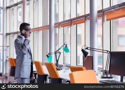 Happy smiling successful African American businessman in a suit in a modern bright office indoors speel on phone