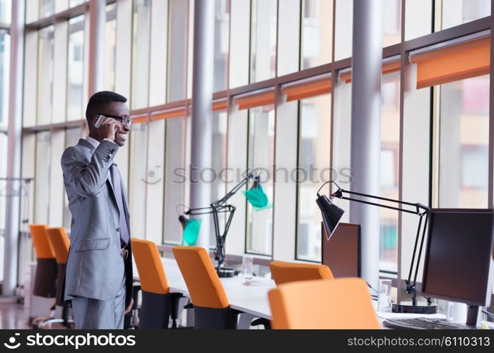 Happy smiling successful African American businessman in a suit in a modern bright office indoors speel on phone