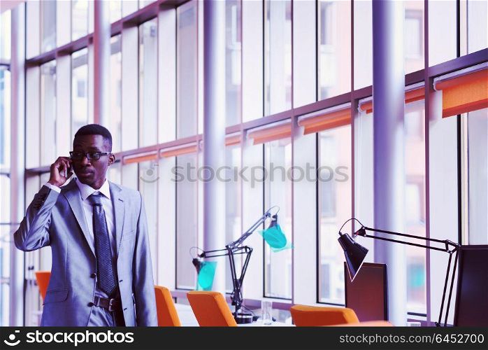 Happy smiling successful African American businessman in a suit in a modern bright office indoors speel on phone