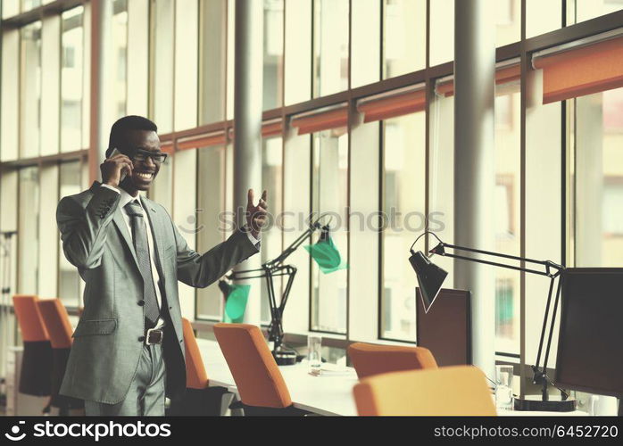 Happy smiling successful African American businessman in a suit in a modern bright office indoors speel on phone