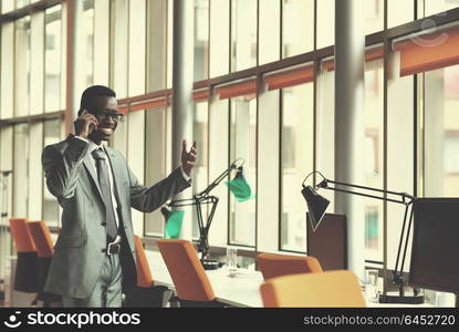 Happy smiling successful African American businessman in a suit in a modern bright office indoors speel on phone