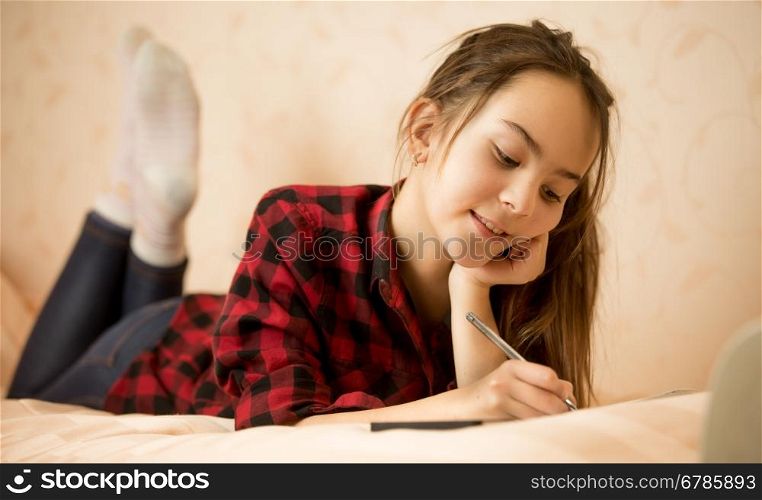 Happy smiling teen girl lying on bed and writing in diary
