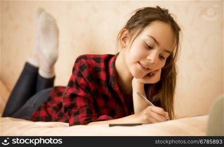Happy smiling teen girl lying on bed and writing in diary