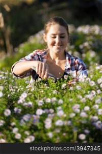 Happy smiling woman cutting flowers at garden at sunny day