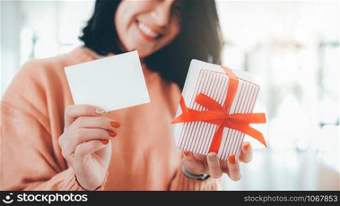 Happy smiling woman holding white blank card and gift box. Blank card for customize text.