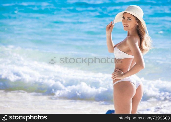 Happy smiling woman in bikini and sunhat on sea beach. Woman in bikini on beach