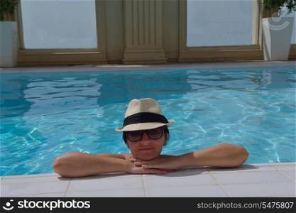 Happy smiling woman with hat and sunglasses in swimming pool at tropical resort