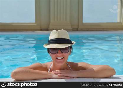Happy smiling woman with hat and sunglasses in swimming pool at tropical resort