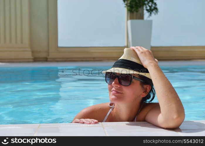 Happy smiling woman with hat and sunglasses in swimming pool at tropical resort