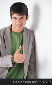 Happy smiling young man leaning against white wall and showing thumbs up