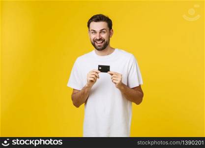 Happy smiling young man showing credit card isolated on yellow background.. Happy smiling young man showing credit card isolated on yellow background