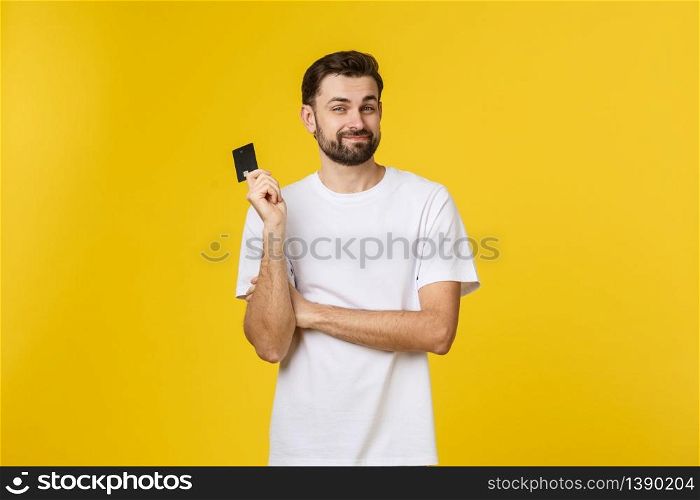 Happy smiling young man showing credit card isolated on yellow background.. Happy smiling young man showing credit card isolated on yellow background