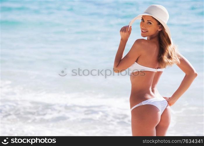 Happy smiling young woman in bikini and sunhat on sea beach. Girl in bikini and sunhat on beach