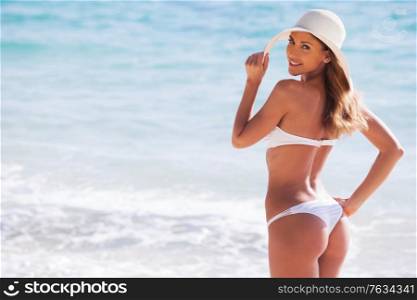 Happy smiling young woman in bikini and sunhat on sea beach. Girl in bikini and sunhat on beach