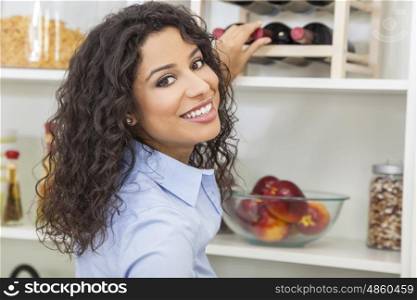 Happy smiling young woman reaching for and choosing bottle of red wine from rack at home