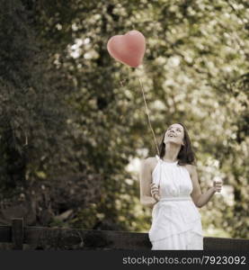 Happy Smiling Young Woman Standing with a Red Shaped Heart Balloon Outdoors