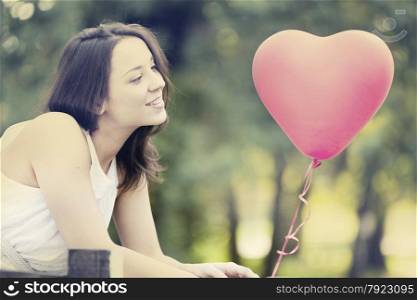 Happy Smiling Young Woman Standing with a Red Shaped Heart Balloon Outdoors