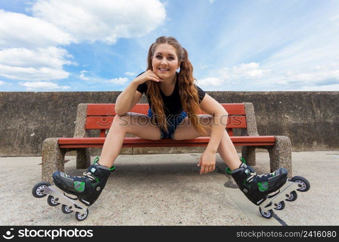 Happy smiling young woman wearing roller skates outdoor. Girl having fun resting on bench.. Smiling girl with roller skates outdoor