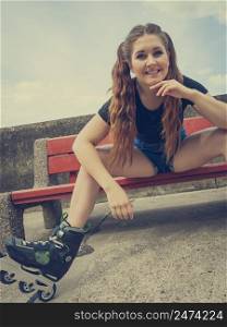 Happy smiling young woman wearing roller skates outdoor. Girl having fun resting on bench.. Smiling girl with roller skates outdoor