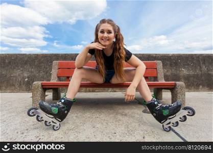 Happy smiling young woman wearing roller skates outdoor. Girl having fun resting on bench.. Smiling girl with roller skates outdoor