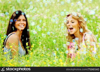 Happy smling girlfriends on green grass field in soap bubbles. Girlfriends on summer grass