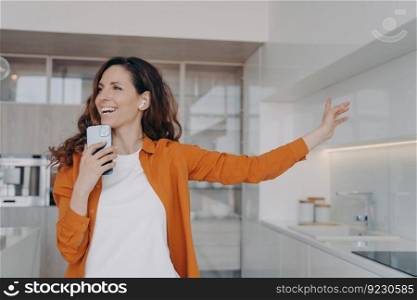 Happy spanish girl in airpods is singing with mobile telephone as with microphone. Woman having fun, relaxing and dancing. Application for music listening online. Housewife is singing song at home.. Happy spanish girl in airpods is singing with mobile telephone as with microphone.