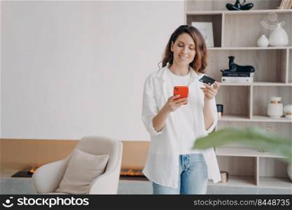 Happy spanish girl is holding credit card and phone. Young pretty woman is going to buy through internet. Girl is booking or purchasing online. Money saving and discount online concept.. Happy spanish girl is holding credit card and phone. Purchasing online, money saving and discount.