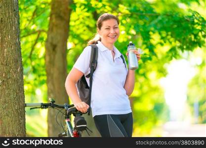 Happy sportswoman with a bottle of water and a bicycle
