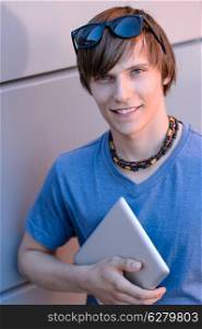 Happy student boy with tablet looking at camera against wall
