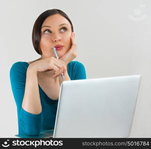 Happy student girl looking up and daydreaming with pan and laptop on grey background. Lots of copyspace