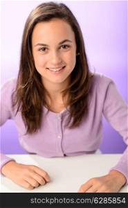 Happy student girl sitting behind desk on purple background portrait