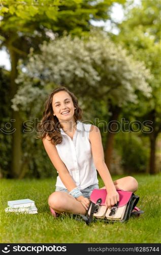 Happy student girl sitting on grass open school bag summer