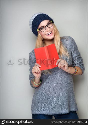 Happy student girl with book in hands wearing stylish hat and glasses isolated on gray background, enrollee of university