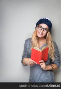 Happy student girl with book in hands wearing stylish hat and glasses isolated on gray background, enrollee of university