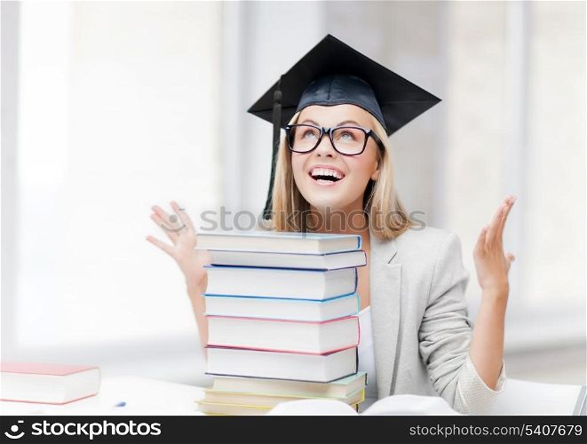 happy student in graduation cap with stack of books