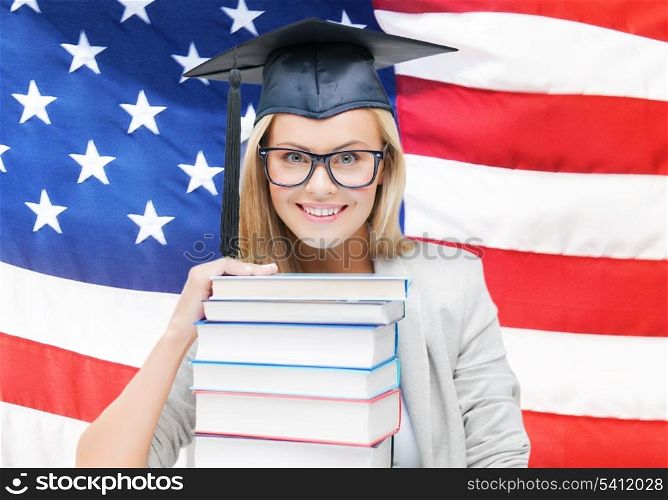 happy student in graduation cap with stack of books over american flag