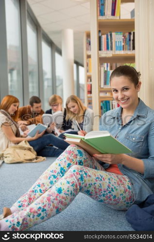 Happy student sitting in school library with classmates in background