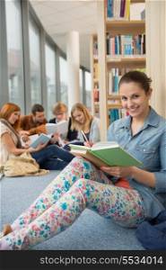 Happy student sitting in school library with classmates in background